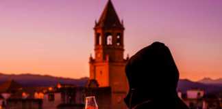 famous spanish drinks a young woman in the hood tasting a Spanish drink on the terrace, view of the church tower and the old town in spain