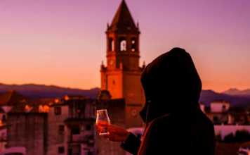 famous spanish drinks a young woman in the hood tasting a Spanish drink on the terrace, view of the church tower and the old town in spain
