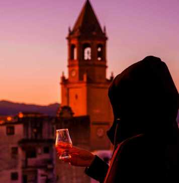 famous spanish drinks a young woman in the hood tasting a Spanish drink on the terrace, view of the church tower and the old town in spain