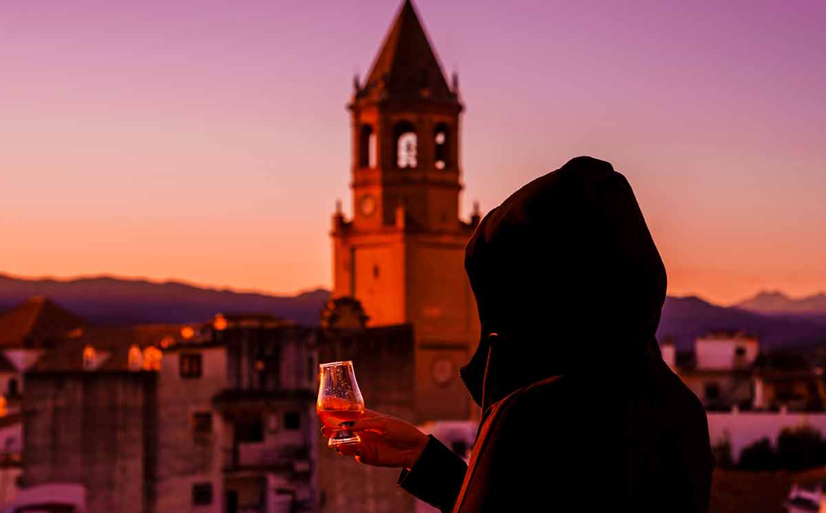 famous spanish drinks a young woman in the hood tasting a Spanish drink on the terrace, view of the church tower and the old town in spain