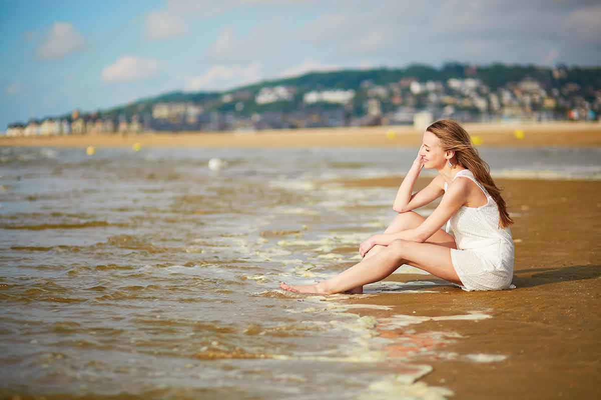 france beaches Beautiful young woman enjoying her vacation by ocean or sea, sitting near water edge at sunset.