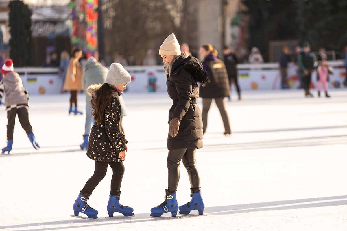 Action Shot Of Beautiful Woman Teaching Her Daughter How To Ice Skate