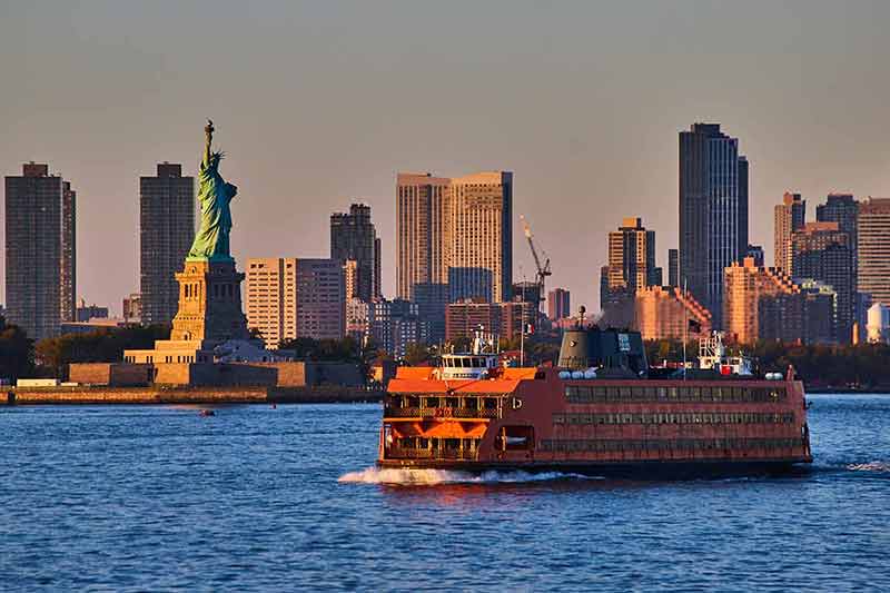 Large Staten Island Ferry Passing By Statue of Liberty In Golden Hour