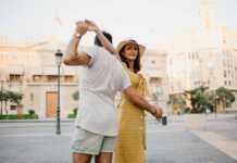 fun things to do in valencia spain A happy girl in a hat and a yellow dress with a plunging neckline is dancing with her boyfriend with a beard and sunglasses in the old town.