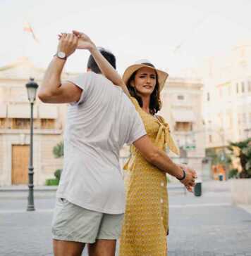 fun things to do in valencia spain A happy girl in a hat and a yellow dress with a plunging neckline is dancing with her boyfriend with a beard and sunglasses in the old town.
