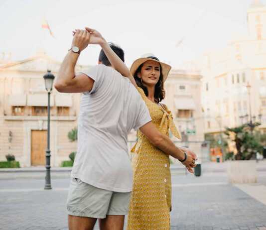 fun things to do in valencia spain A happy girl in a hat and a yellow dress with a plunging neckline is dancing with her boyfriend with a beard and sunglasses in the old town.