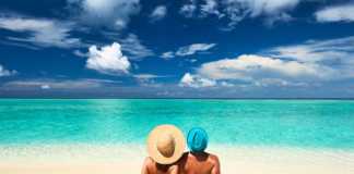 glowing beaches maldives man and woman sitting on the sand facing the ocean wearing hats