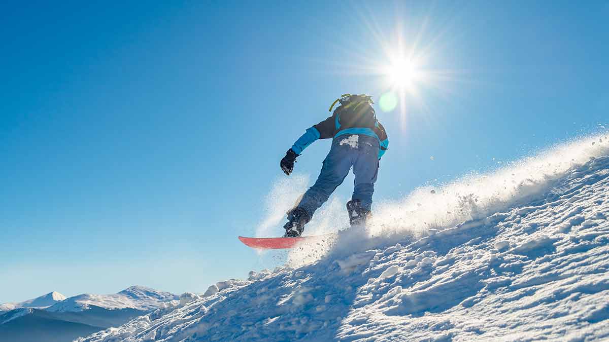 Snowboarder Riding Snowboard In Mountains At Sunny Day