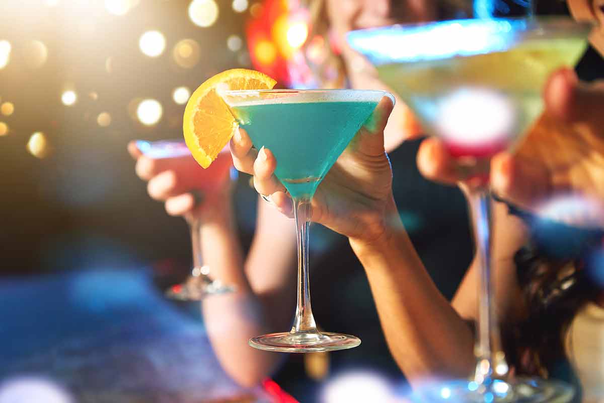 three female hands drinking colourful cocktails