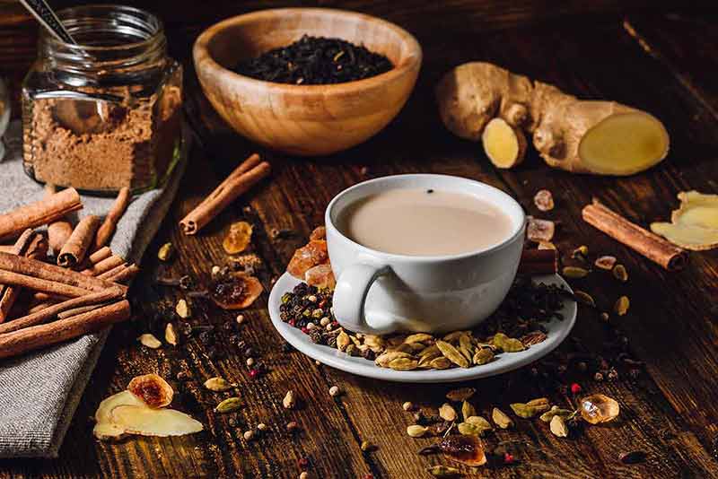 indian chai drinks cup of chai with ingredients strewn on a wooden table