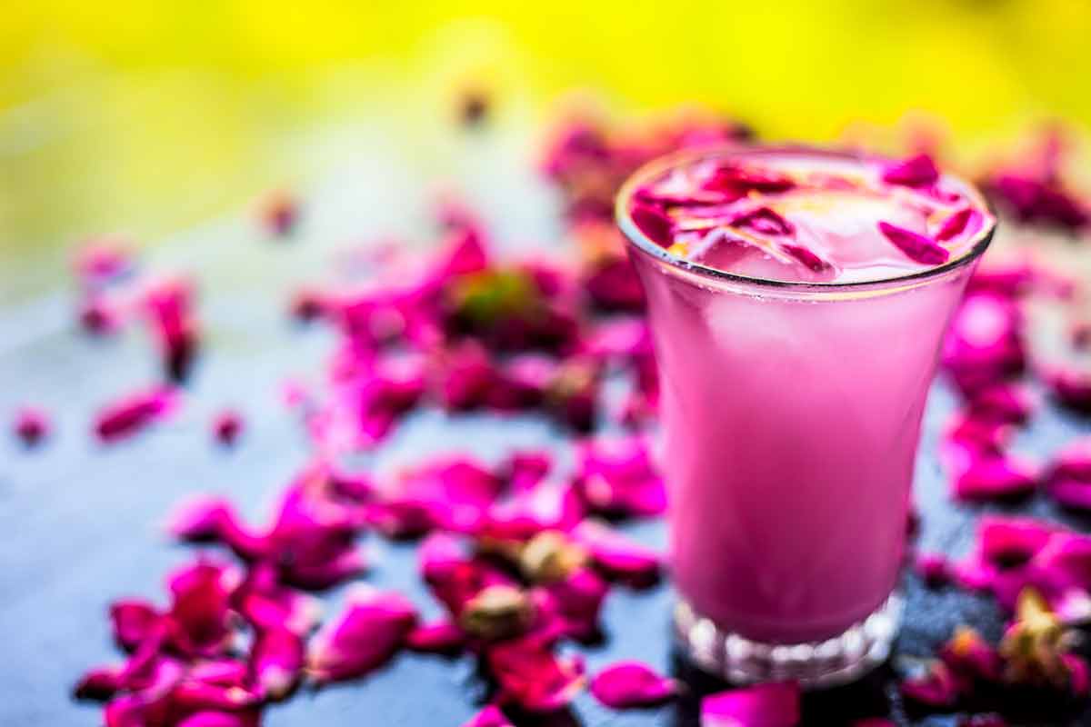 indian summer drinks glass with pink drink with some rose petals on black colored shiny surface.