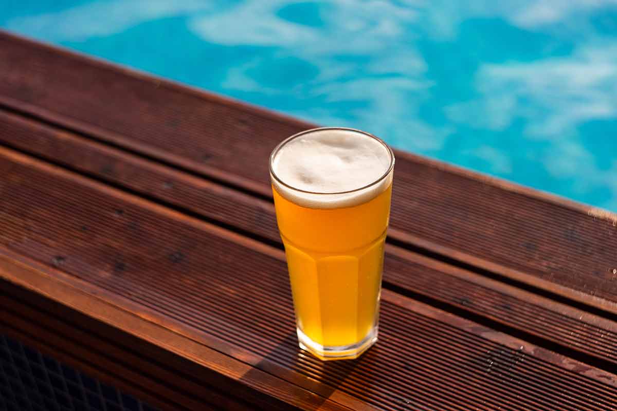 jamaican alcoholic drinks pint glass of cold lager beer sitting on edge of blue swimming pool