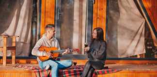 maine glamping couple drinking wine and playing guitar on tent verandah