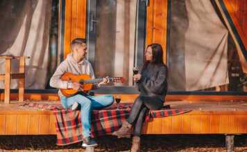 maine glamping couple drinking wine and playing guitar on tent verandah