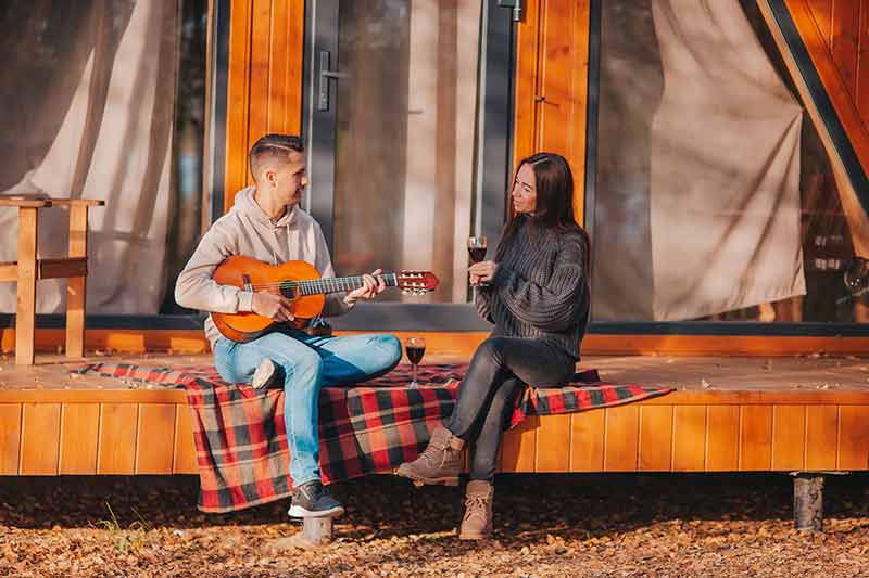 maine glamping couple drinking wine and playing guitar on tent verandah