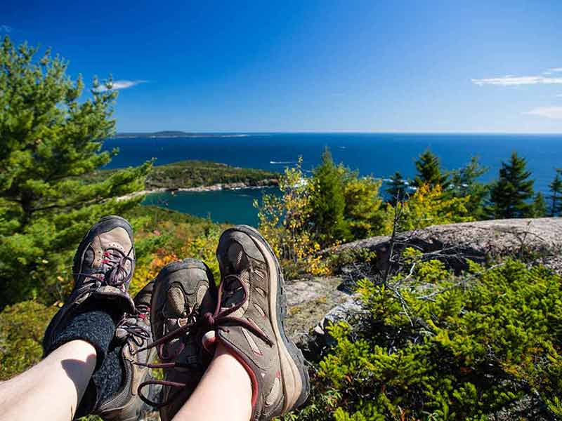 maine national parks camping two sets of sneakered legs Resting at the top of a mountain in Acadia National Park