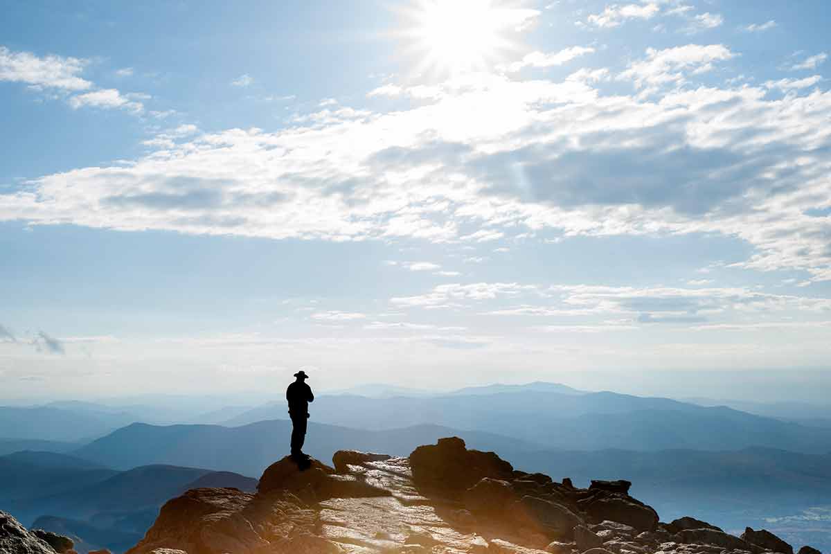 major landmarks in new hampshire Sun filtered by clouds hits the rocky top on Mount Washington and the silhouette of man