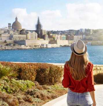 back of woman wearing a hat looking at the view of Malta over the water