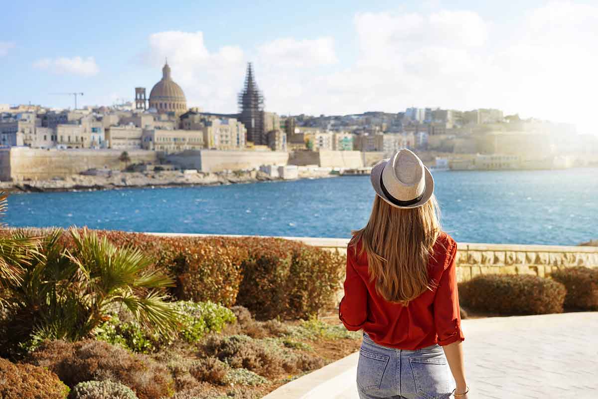 back of woman wearing a hat looking at the view of Malta over the water