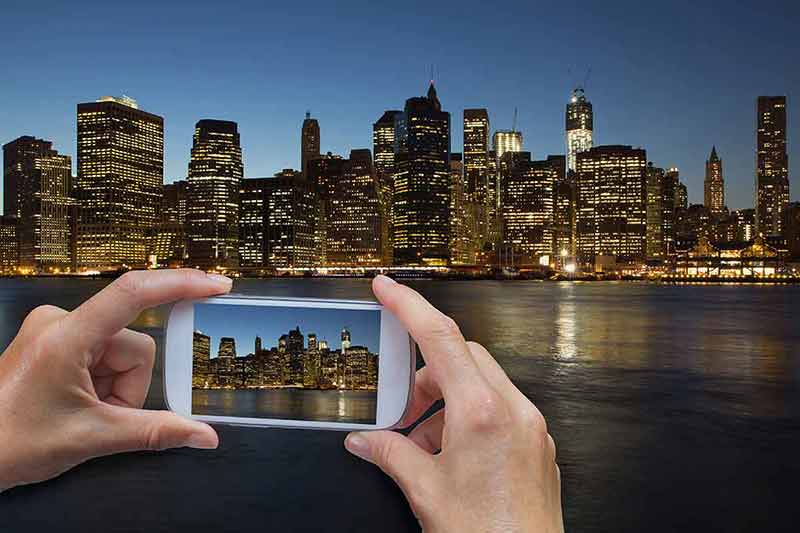 manhattan at night wallpaper In the bottom left of the photo are hands holding smart phone and taking picture of Lower Manhattan in New York City at night (USA).
