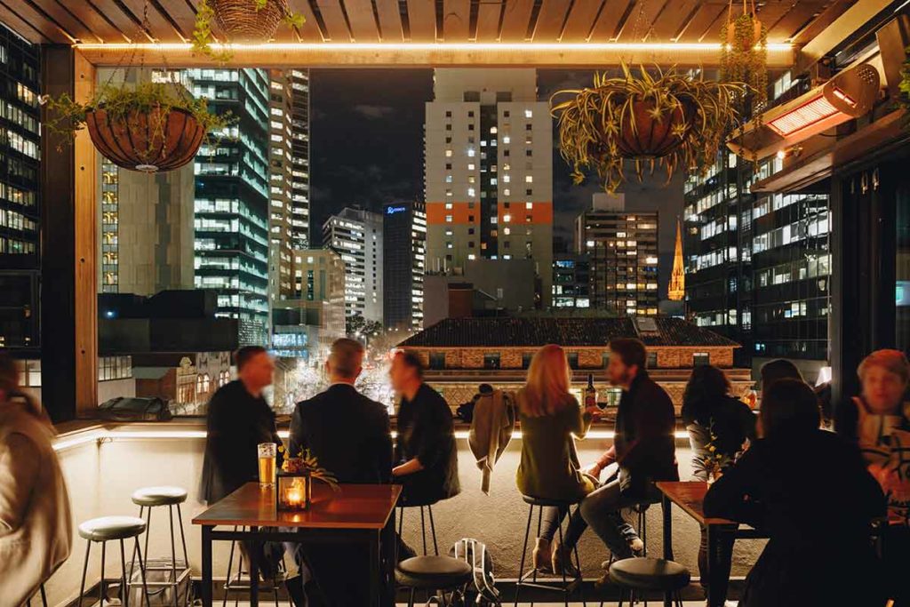 People looking for things to do in Melbourne Saturday night in a bar with a fantastic view of Melbourne at night