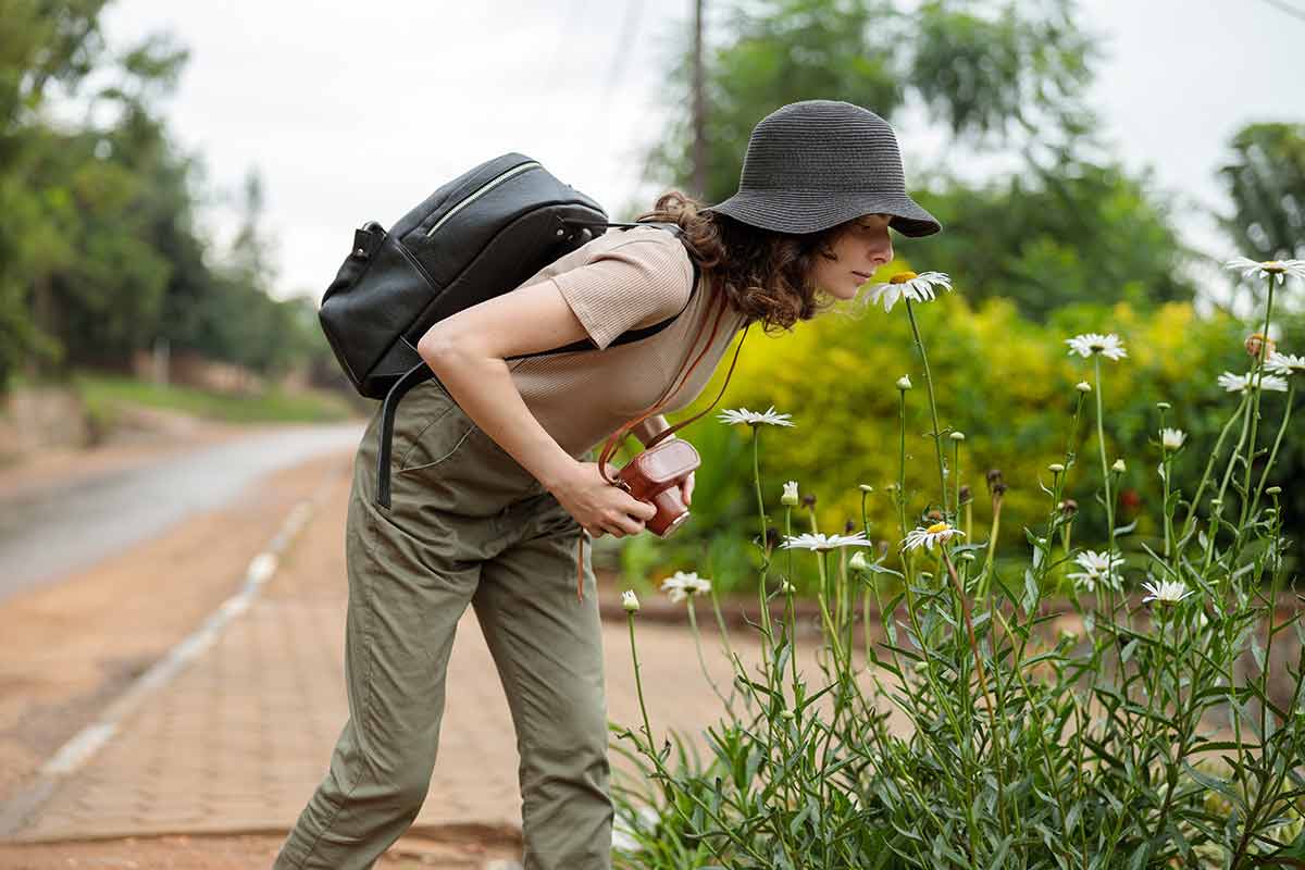 woman photographing flowers with minimalist backpack on her back