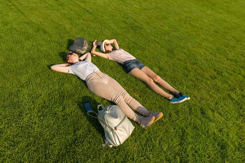 two grils lying on a lawn with minimalist backpacks