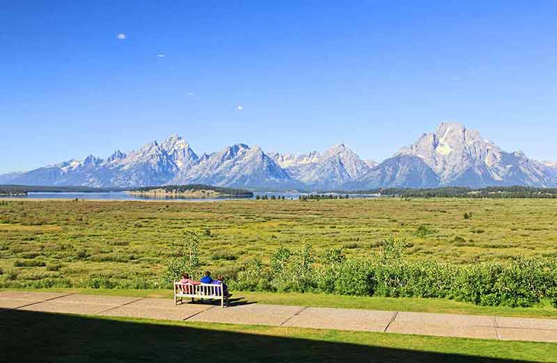 monuments and national parks in wyoming three people sitting on a bench admiring the view of the mountains