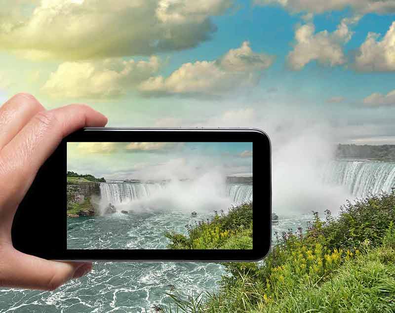 Female hand with smartphone taking a picture of Niagara Falls.