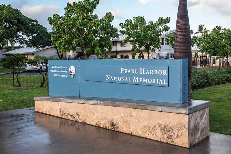 national parks in hawaii list Pearl Harbor National Memorial welcome sign has white letters on blue background under white cloudscape with green lawn in back. Some low level buildings.
