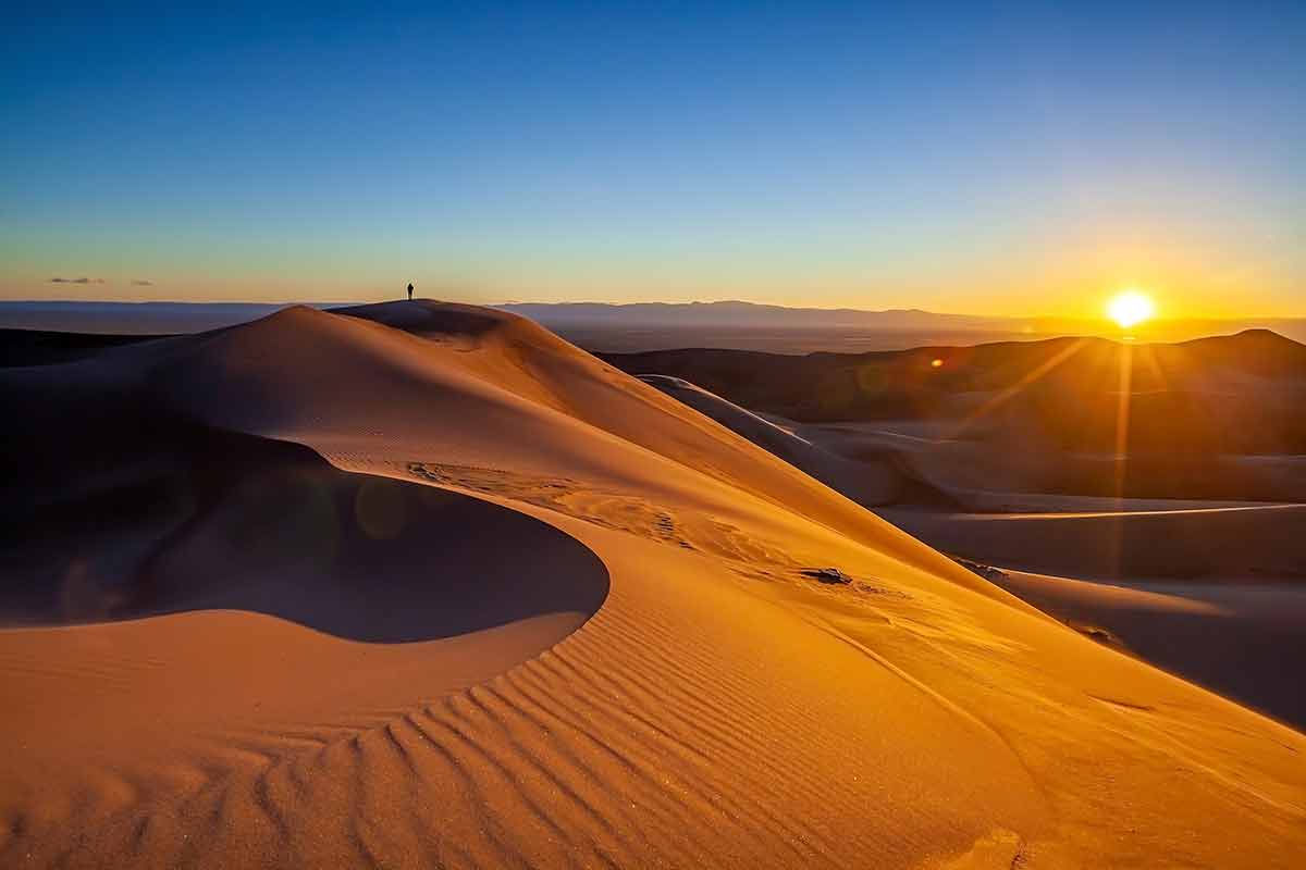 national parks near denver colorado a small figure standing in the distance on a giant dune at sunset
