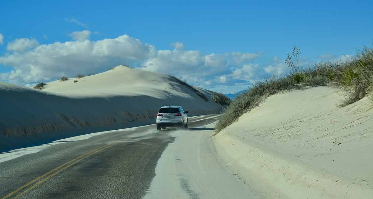 national parks new mexico white car driving on a road past the sand dunes