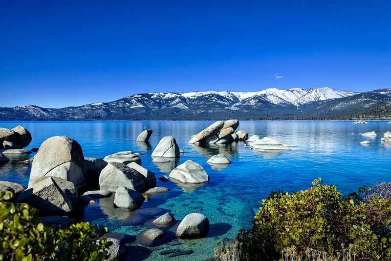 rocks in clear water with snowcapped mountains in the background