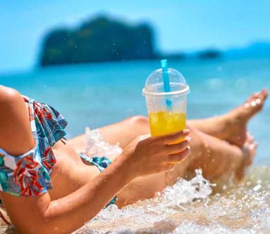 nice beaches in malaysia A beautiful slender girl in a swimsuit enjoys a tan while lying on a tropical beach, holding a glass of pineapple juice in her hand