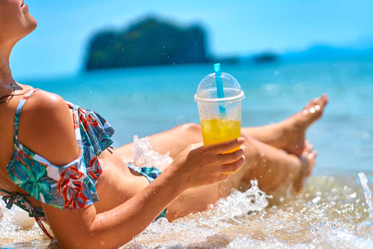 nice beaches in malaysia A beautiful slender girl in a swimsuit enjoys a tan while lying on a tropical beach, holding a glass of pineapple juice in her hand