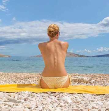 nude beaches croatia Rear view of relaxed sexy young caucasian woman sitting on yellow towel, sunbathing topless alone on romote pabble beach on Pag island