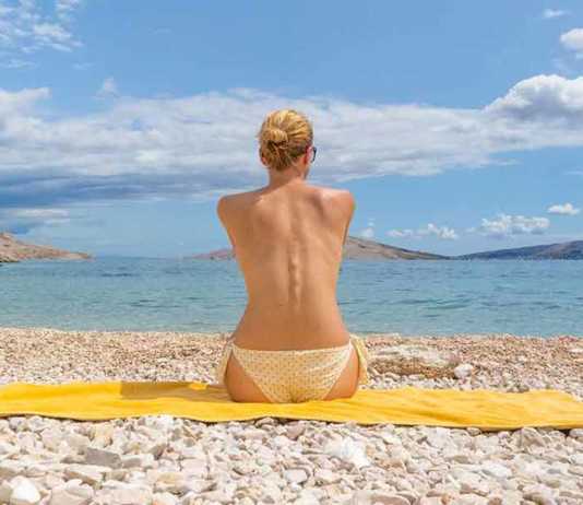 nude beaches croatia Rear view of relaxed sexy young caucasian woman sitting on yellow towel, sunbathing topless alone on romote pabble beach on Pag island