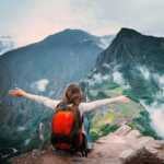 View of girl sitting on the edge of the rock with raised hands and taking pleasure of forested mountains landscape of Machu Picchu.