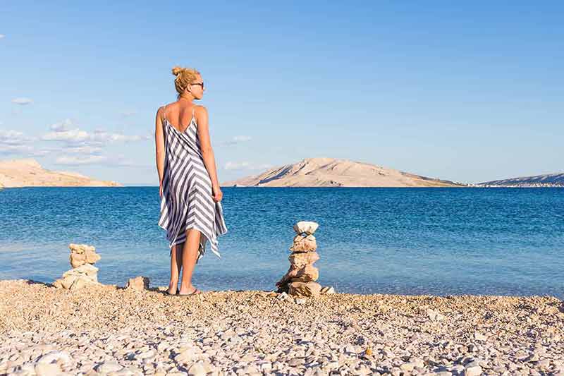 sandy beaches in croatia Happy carefree woman wearing beautiful striped summer dress enjoying late afternoon walk on white pabbled beach