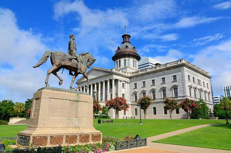 south carolina state house on a blue-sky day with a statue of a man on a horse in front of the building