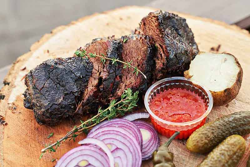 texas day trips from austin Fresh prepared meat with rosemary potatoe onion and red sauce on a wooden plate.