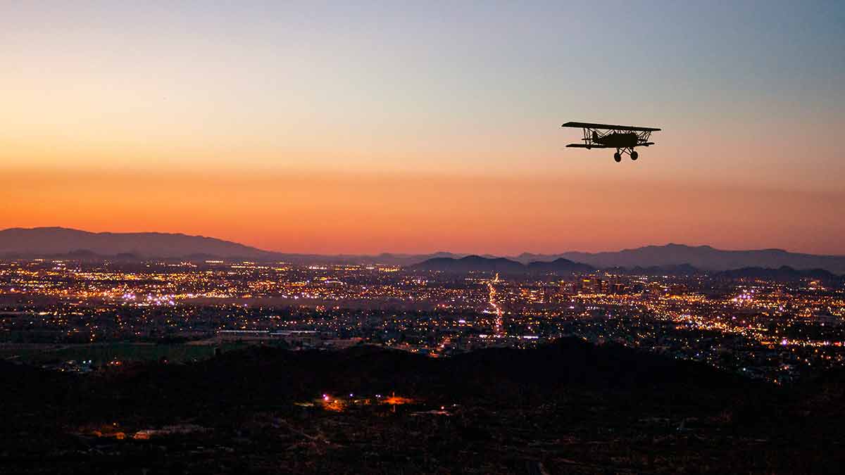 things to do at night in phoenix az orange sunset with silhouette of a biplane flying over the city