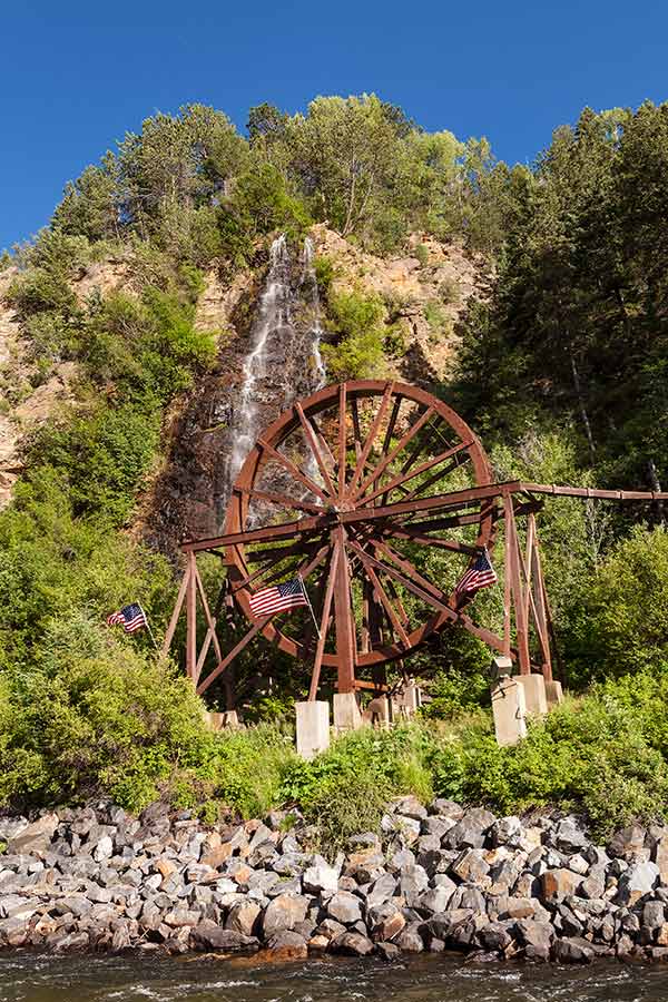 things to do idaho springs water wheel with American flags on a blue-sky day