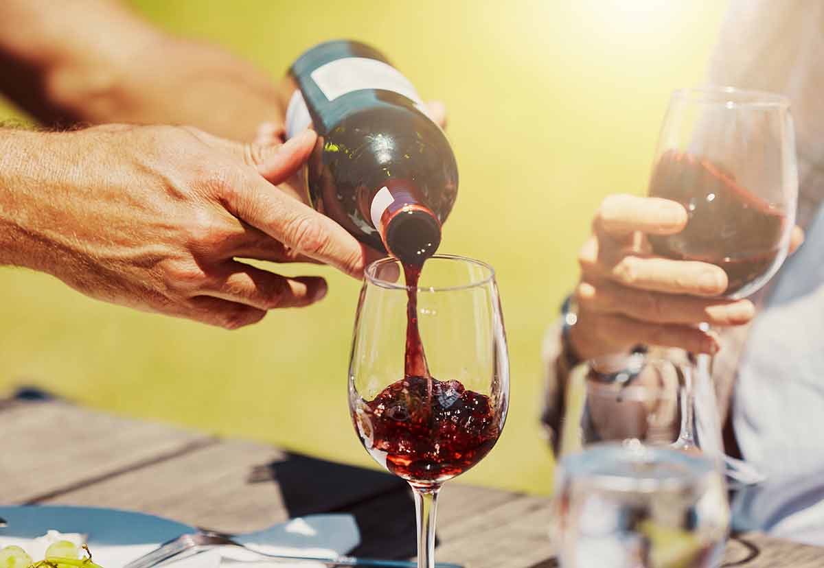 Closeup Of Unknown Farmer Pouring Red Wine Into Wineglass On Farm For Friends