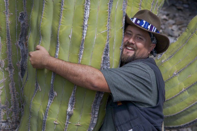 a man with his arms around a giant cactus