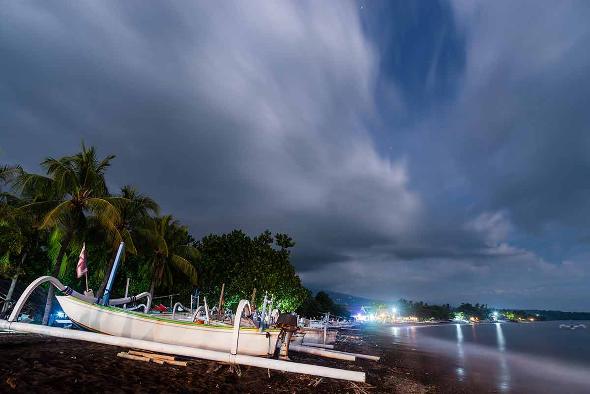 Amed Beach At Night In Bali, Indonesia. Long exposure photography resulting in motion blur in the clouds, the sea and the trees.