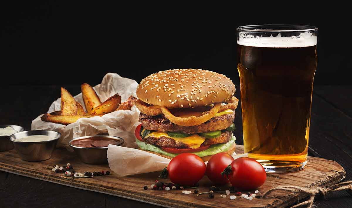 classic American burgers with hot grilled patty, melted cheese, tomatoes, onion, sauces, fried chips and beer.