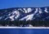 20 Things To Do In Big Bear For The Perfect Mountain Escape Snow-covered ski slopes form the backdrop for Big Bear, California with Big Bear Lake in the foreground.