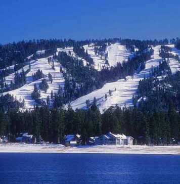 20 Things To Do In Big Bear For The Perfect Mountain Escape Snow-covered ski slopes form the backdrop for Big Bear, California with Big Bear Lake in the foreground.