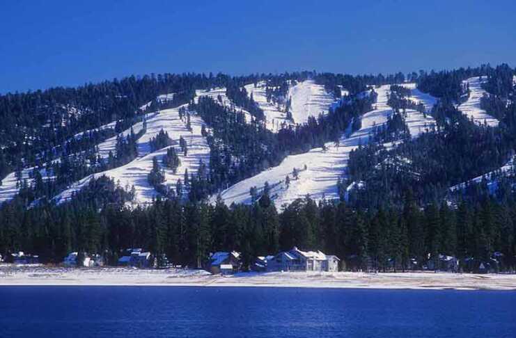 20 Things To Do In Big Bear For The Perfect Mountain Escape Snow-covered ski slopes form the backdrop for Big Bear, California with Big Bear Lake in the foreground.